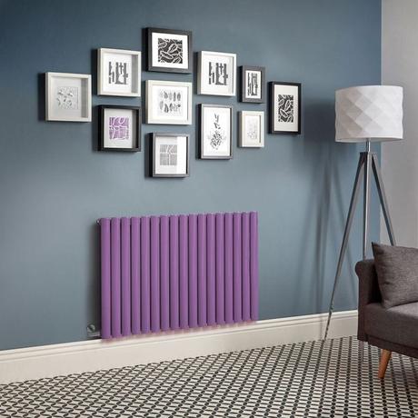 Milano Aruba electric lush purple horizontal designer radiator on blue wall beneath multiple pieces of framed artwork nearby freestanding lamp and dark gray settee