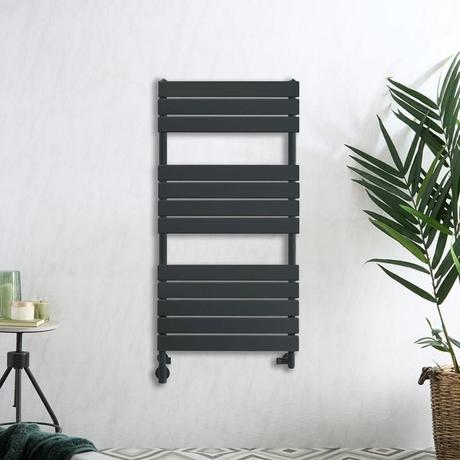 Milano Lustro anthracite dual fuel flat panel heated towel rail on white wall nearby houseplant and small table with candle and other items