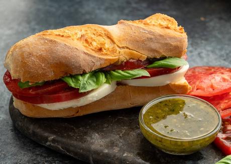a caprese sandwich sitting with a jar of pesto on a stone cutting board