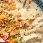 close up image of white bean chili and silver spoon in blue bowl
