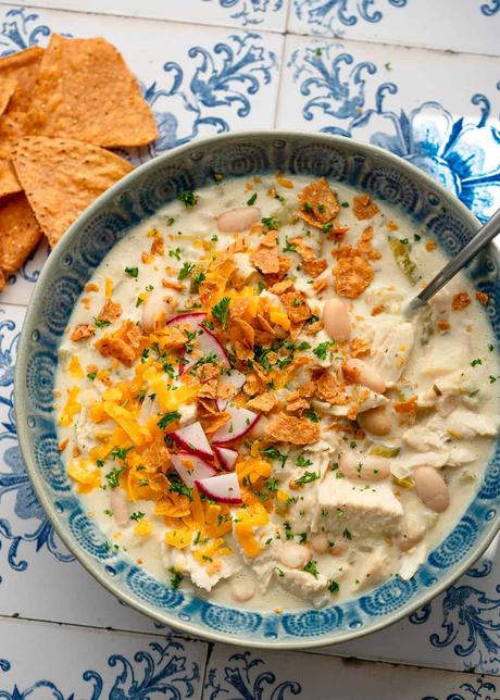 overhead image of white bean chili in blue bowl with spoon on decorative background