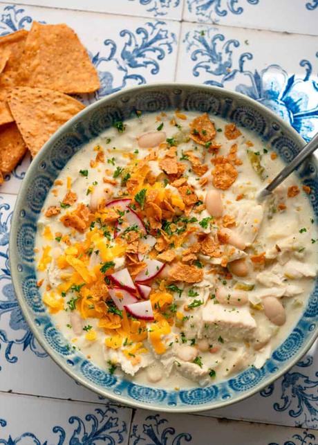 overhead image of white bean chili in blue bowl with spoon on decorative background