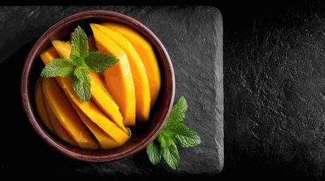 Fresh sliced mangoes served in a bowl with mint leaves showcasing bright yellow pulp and summer fruit presentation