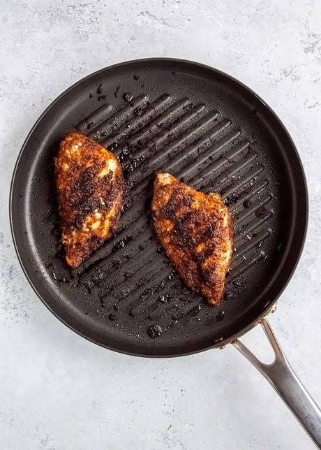 two chicken breasts cooking in a skillet