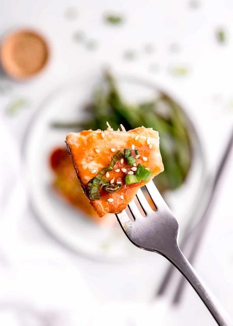close up image of a bite of baked salmon on a fork with white plate in background