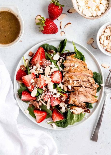 garnished strawberry spinach salad on a white plate