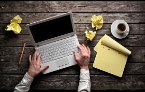 Laptop with blank notepad and pencil with sheets of crumpled pap