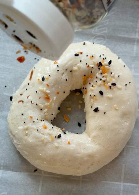 bagels being sprinkled with everything bagel seasoning
