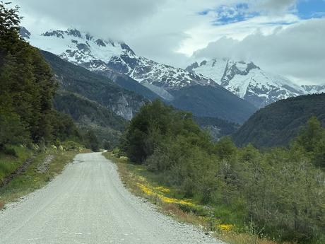 Remote gravel section of the Carretera Austral winding through forest towards snow-covered mountains in Chilean Patagonia