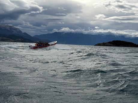 Small tour boat crossing the choppy waters of Lago General Carrera in Chilean Patagonia beneath dramatic cloud-covered mountains