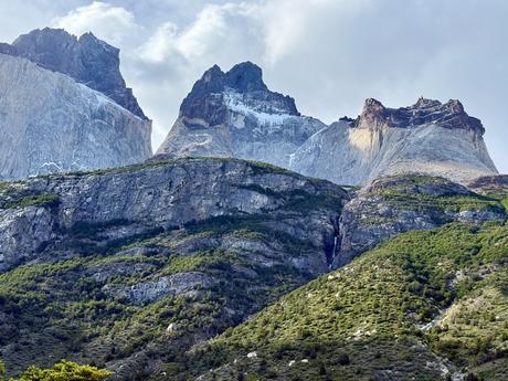 Granite peaks of the Cuernos del Paine and a distant waterfall above forested slopes on the W Trek