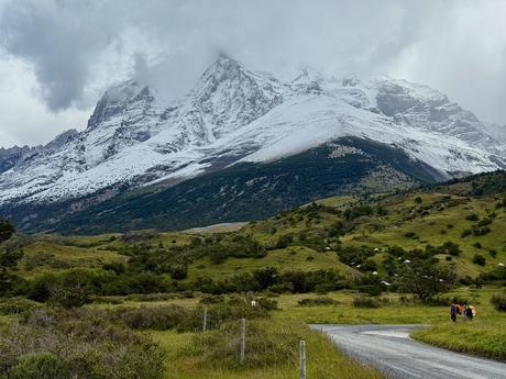 Hikers following a gravel road beneath cloud-covered, snow-dusted mountains on the Torres del Paine W Trek near Refugio Central