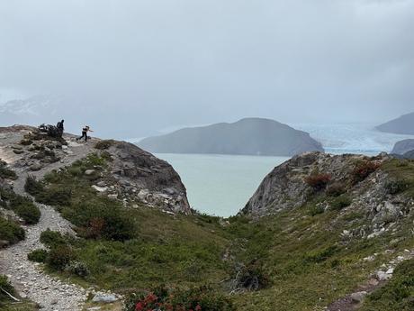 Hikers battling extremely high winds to cross a rocky ridge overlooking Grey Lake and Grey Glacier on the W Trek