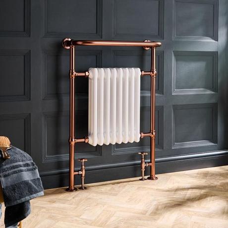 Milano Elizabeth brushed copper traditional heated towel rail on wooden flooring in front of dark gray wall