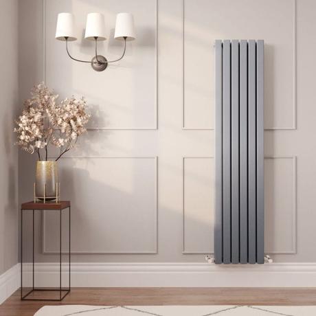 Milano Capri silver flat panel vertical designer radiator on light beige wall nearby table with vase and fake houseplant beneath triple lamp fitting