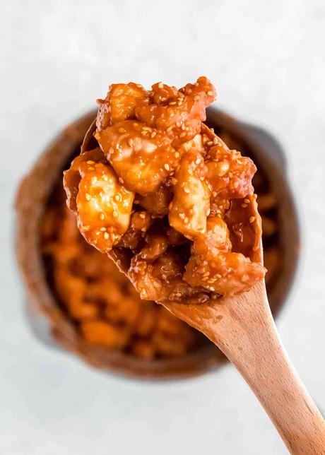 a wooden spoon full of crispy, saucy sesame chicken