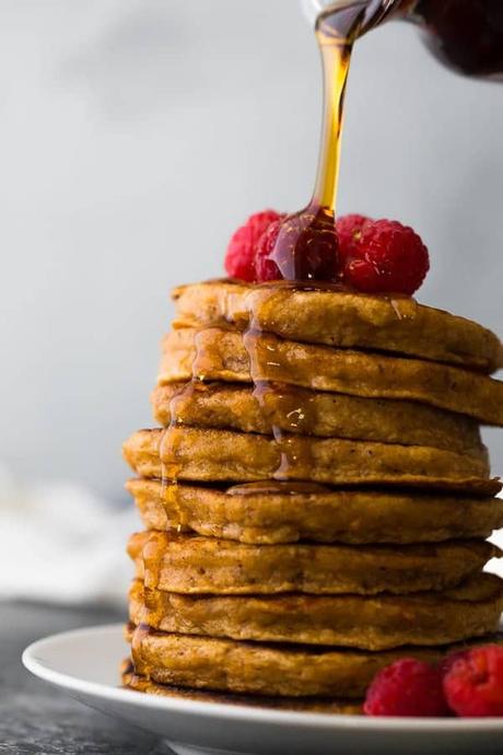 stack of sweet potato pancakes with fresh raspberries and syrup being drizzled over top
