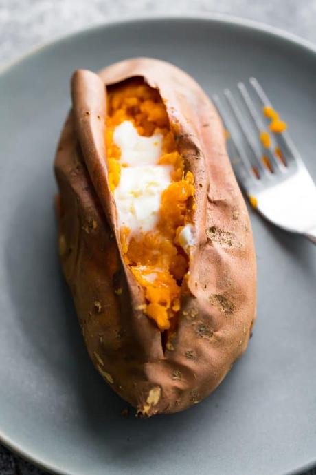 baked sweet potato with butter on gray plate with a fork