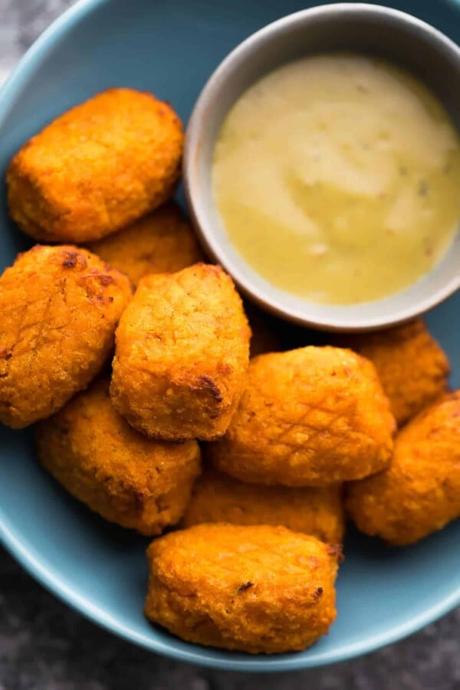 a pile of crispy air fryer sweet potato tots with dipping sauce on blue plate
