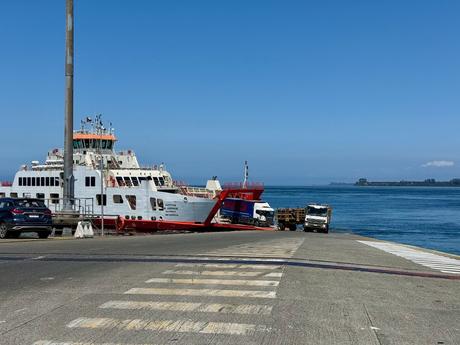 Vehicle ferry docked at a loading ramp in southern Chile, with lorries and cars boarding beside the water.