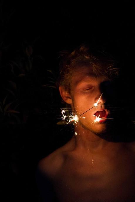 man without shirt lit by sparkler