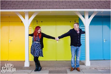 couple holding hands in front of rainbow coloured beach huts