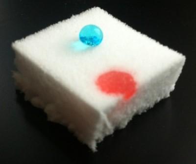 Demonstration of the oleophilic and at the same time hydrophobic properties of a silylated nanocellulose sponge: A droplet of water (blue) sits on the surface, whereas a droplet of oil (red) is absorbed by the material.