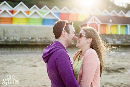 cute couple cuddle in front of rainbow beach huts in Scarborough