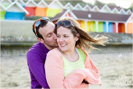 Couple cuddles in front of rainbow beach huts in fun engagement photography session