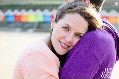 Couple cudding on the beach in engagement photos in front of rainbow beach huts