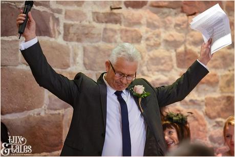Father of the bride holds up arms during speeches at the ashes