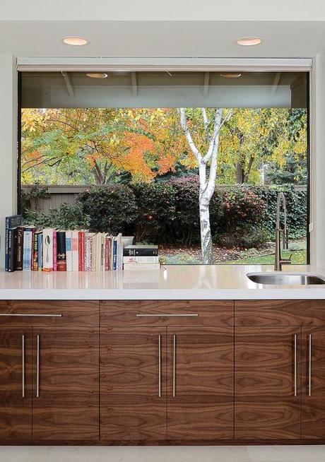 Kitchen with wood cabinets and white countertops with window overlooking a backyard.